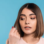 Kobieta z cienkimi włosami trzymająca pasmo włosów, zastanawiająca się nad pielęgnacją i sposobami na dodanie objętości