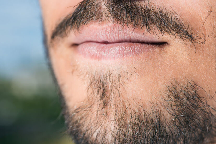 Zbliżenie na twarz mężczyzny z rzadkim zarostem, ukazujące nieregularny wzrost włosów na brodzie i wąsach